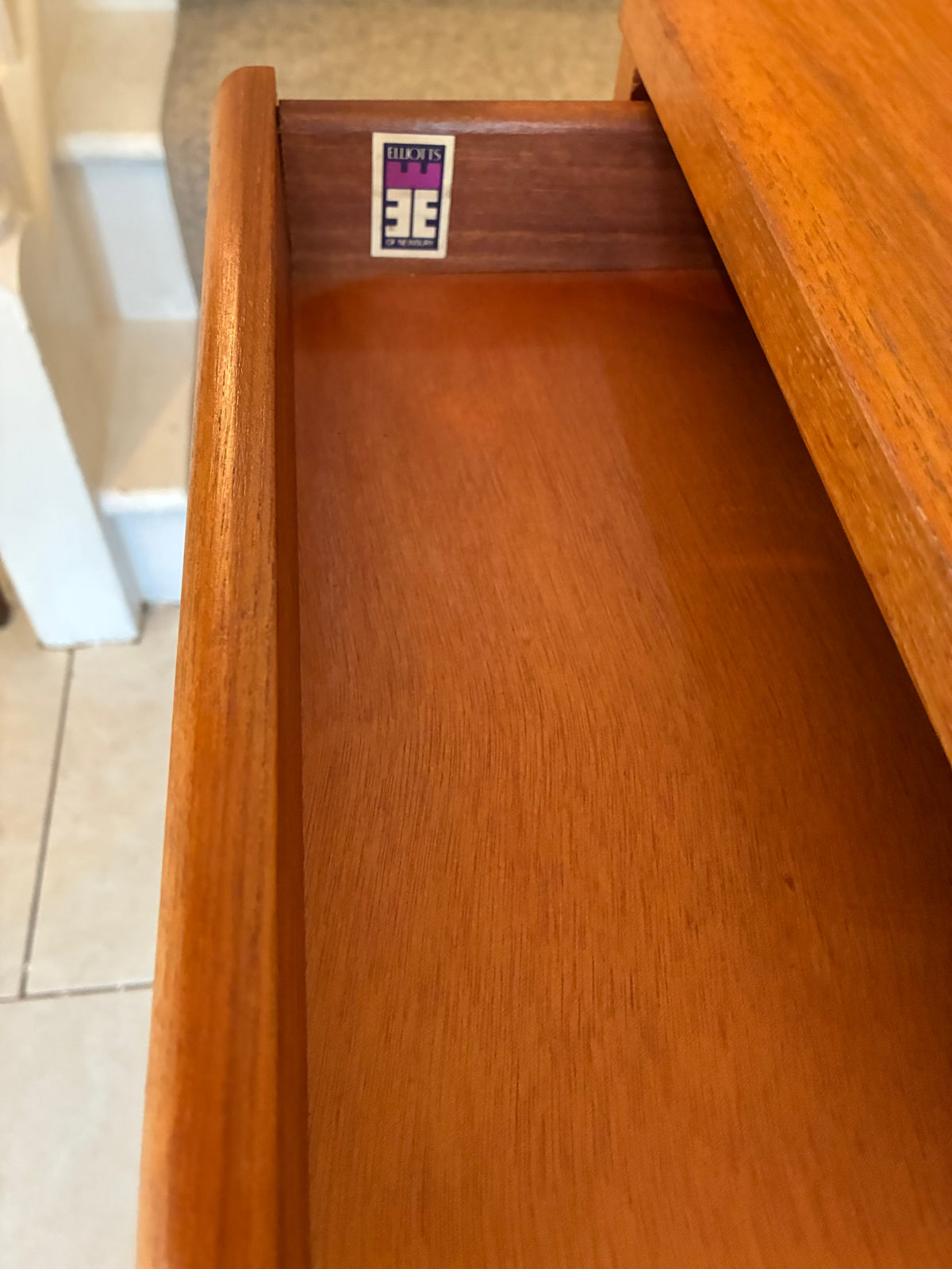 Close-up of an open wooden drawer showing a warm reddish-brown wood finish and a small interior label sticker near the top.