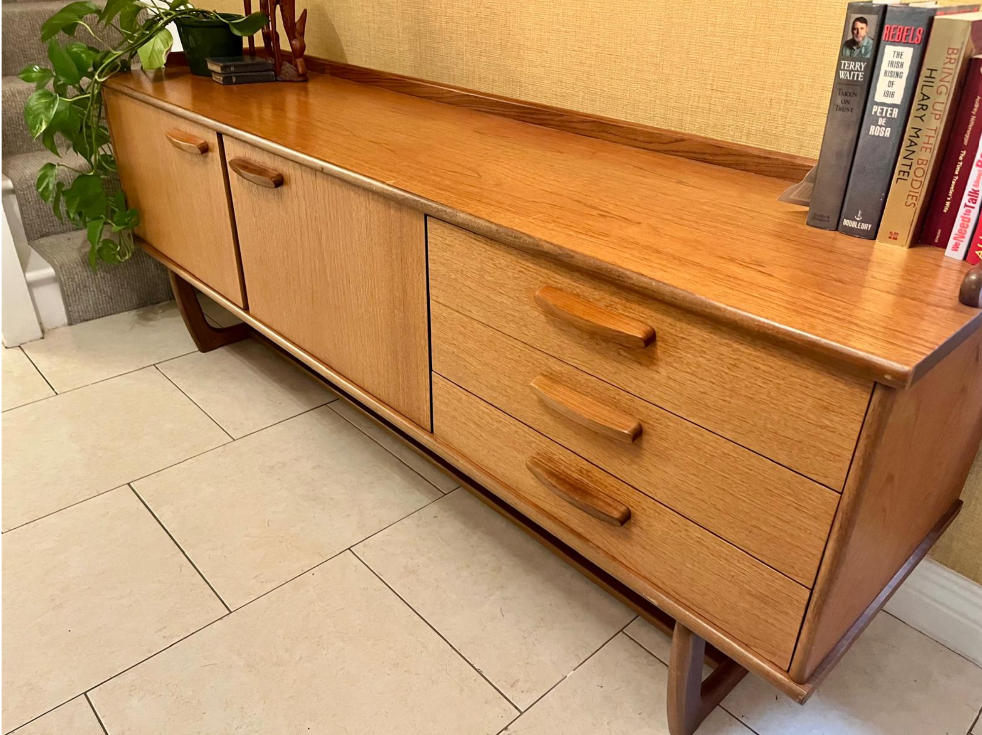 Mid-century modern wooden sideboard with a warm honey finish, featuring three cabinet doors on the left and three drawers on the right, with matching wood handles and angled legs.