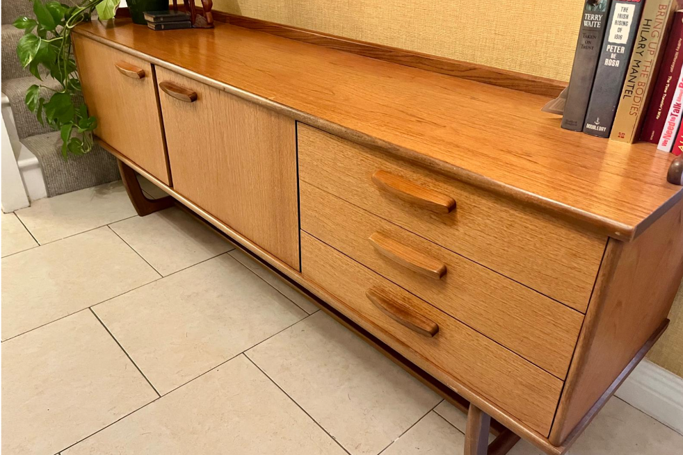 Mid-century modern wooden sideboard with a warm honey finish, featuring three cabinet doors on the left and three drawers on the right, with matching wood handles and angled legs.
