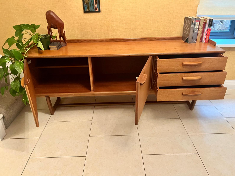 Mid-century modern wooden sideboard with a warm honey finish, featuring three cabinet doors on the left and three drawers on the right, with matching wood handles and angled legs.