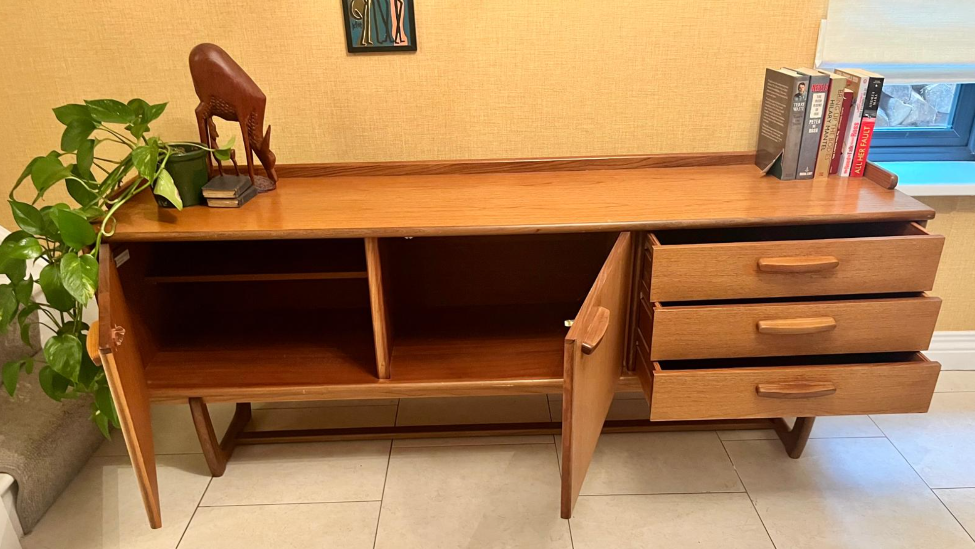 Mid-century modern wooden sideboard with a warm honey finish, featuring three cabinet doors on the left and three drawers on the right, with matching wood handles and angled legs.