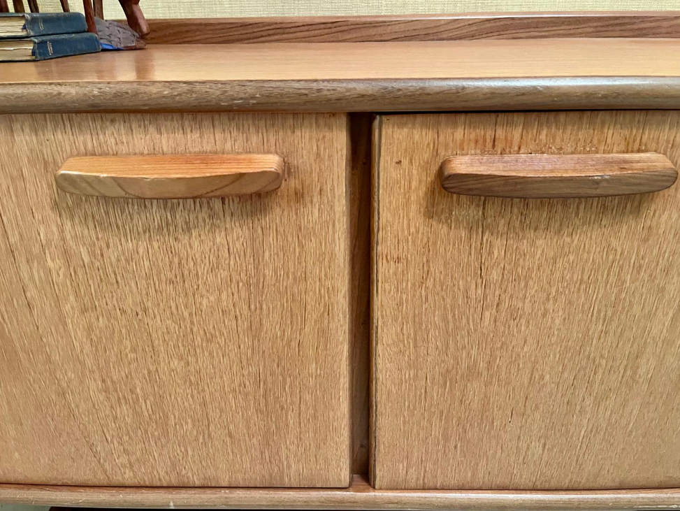 Mid-century modern wooden sideboard with a warm honey finish, featuring three cabinet doors on the left and three drawers on the right, with matching wood handles and angled legs.