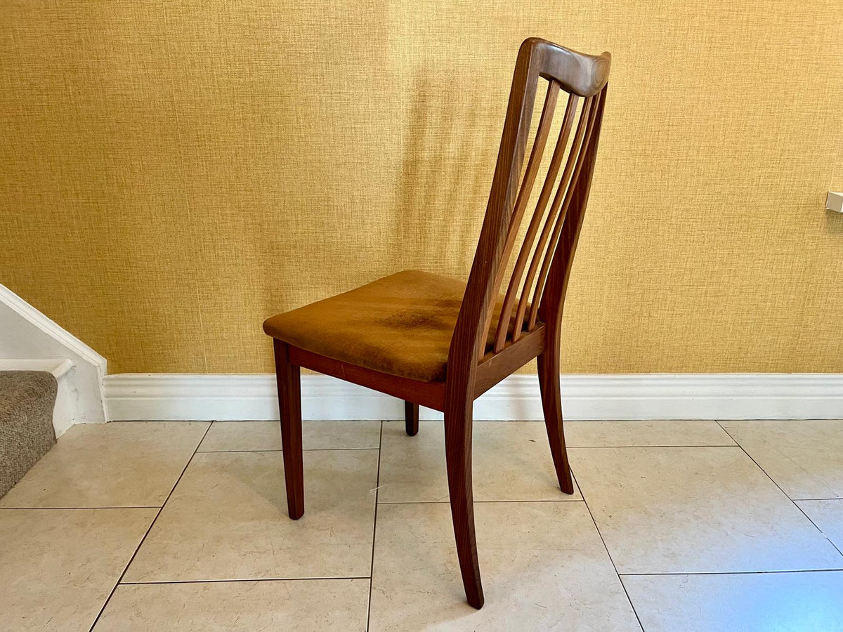 a mid-century G Plan modern wooden dining chair with vertical slat backs and brown velvet seats, arranged on a tiled floor against a textured yellow wall.