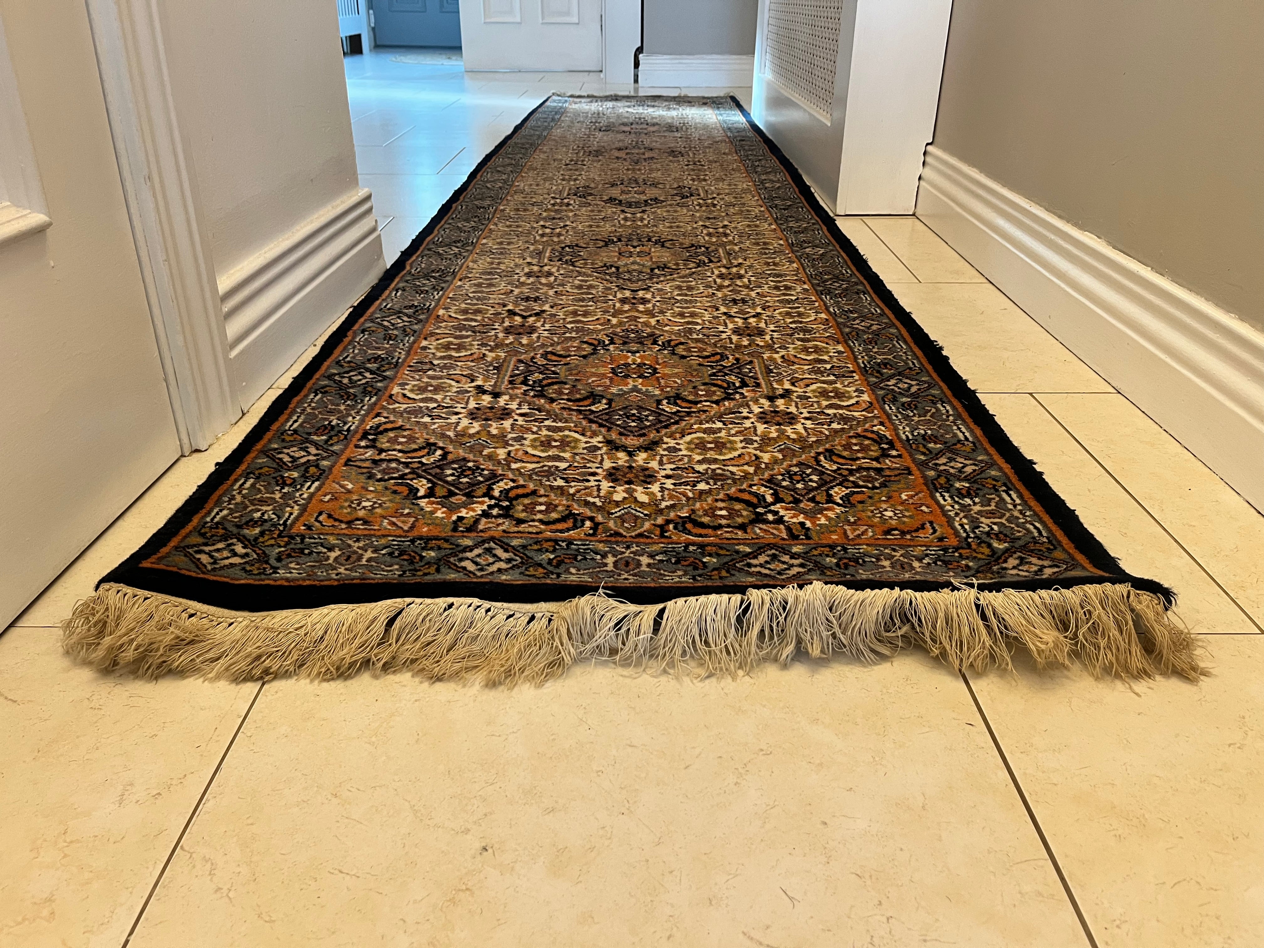 A long traditional vintage runner rug with beige and black fringe, displayed on a light tiled hallway floor y Grace & Joy Furniture