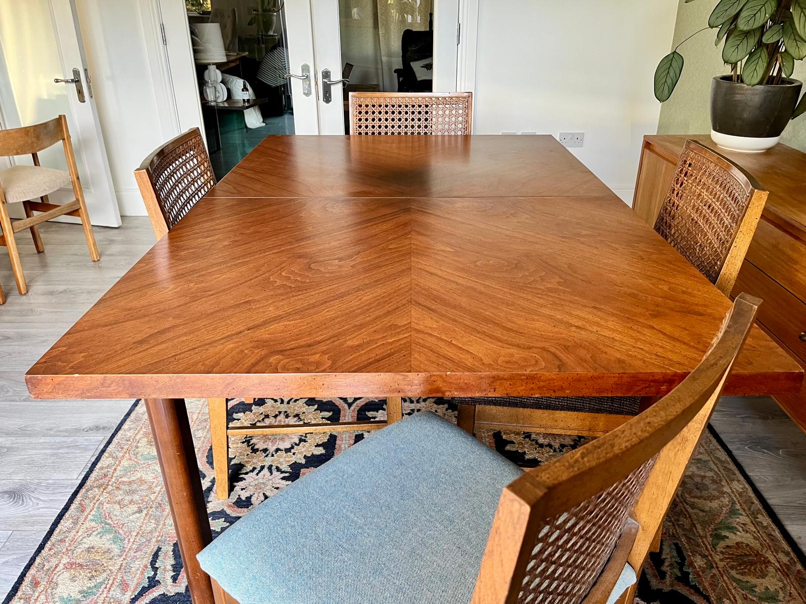 A wooden dining table by Lane with a herringbone patterned top and matching woven-back chairs, shown in a home dining room setting with a patterned rug and potted plant.