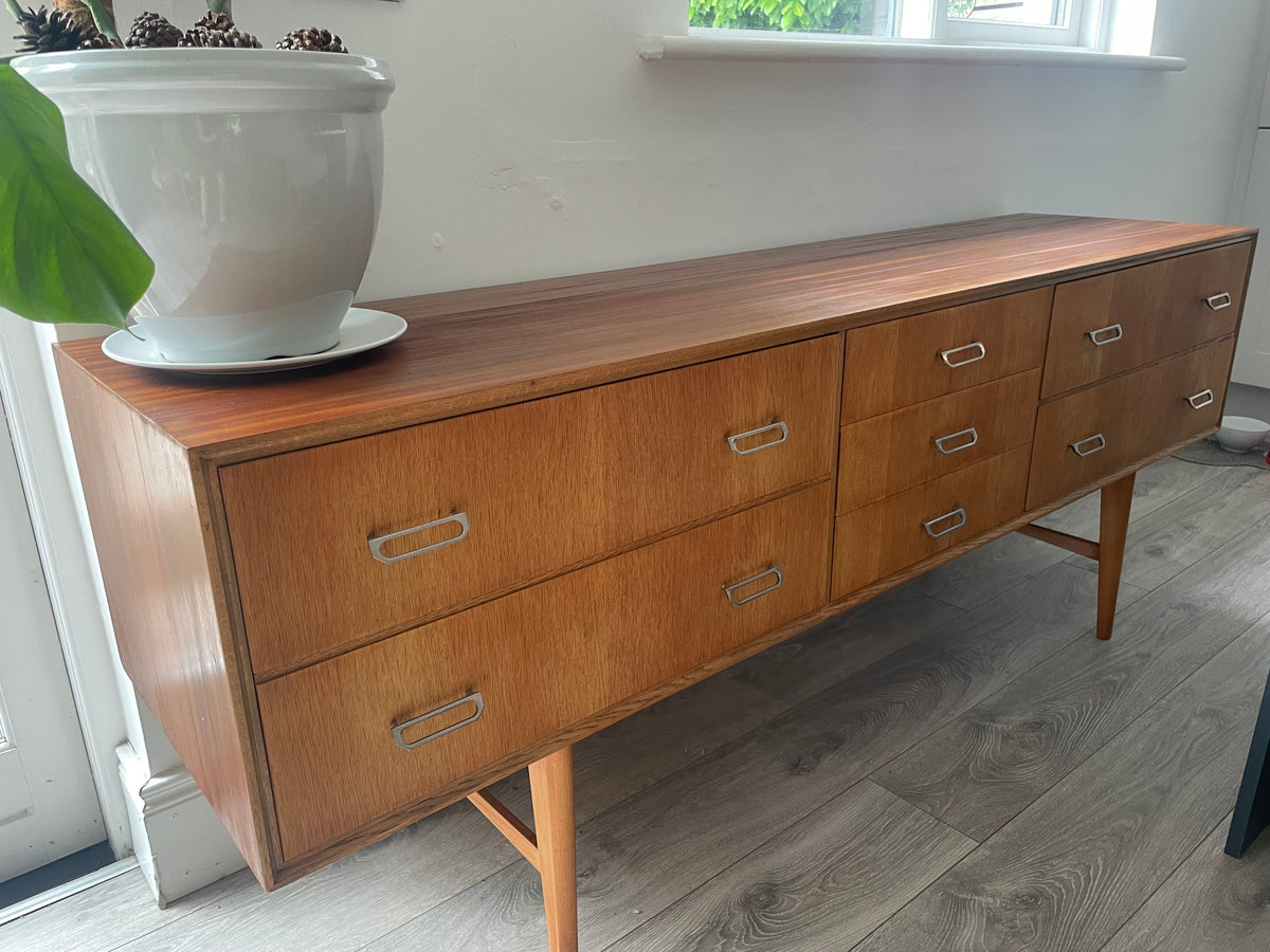 Mid-century modern wooden meredew credenza with six drawers and silver handles, shown in a styled room with gray wood floors, a green wall, and a mirror behind it.