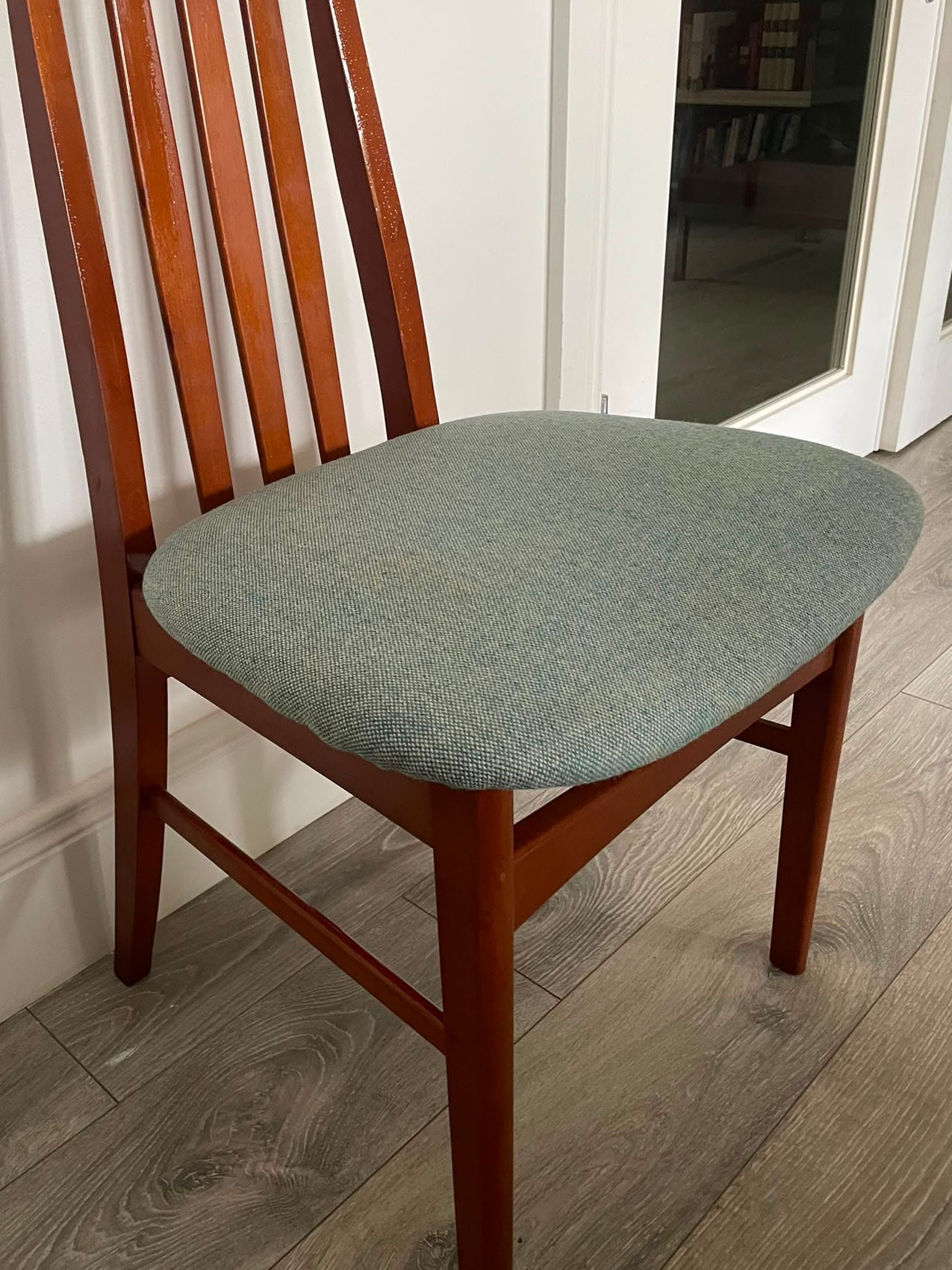 A wooden mid century Jenitique dining chair with a tall slatted backrest and a light blue upholstered seat cushion, shown on a gray wood floor against a white wall by Grace & Joy Furniture
