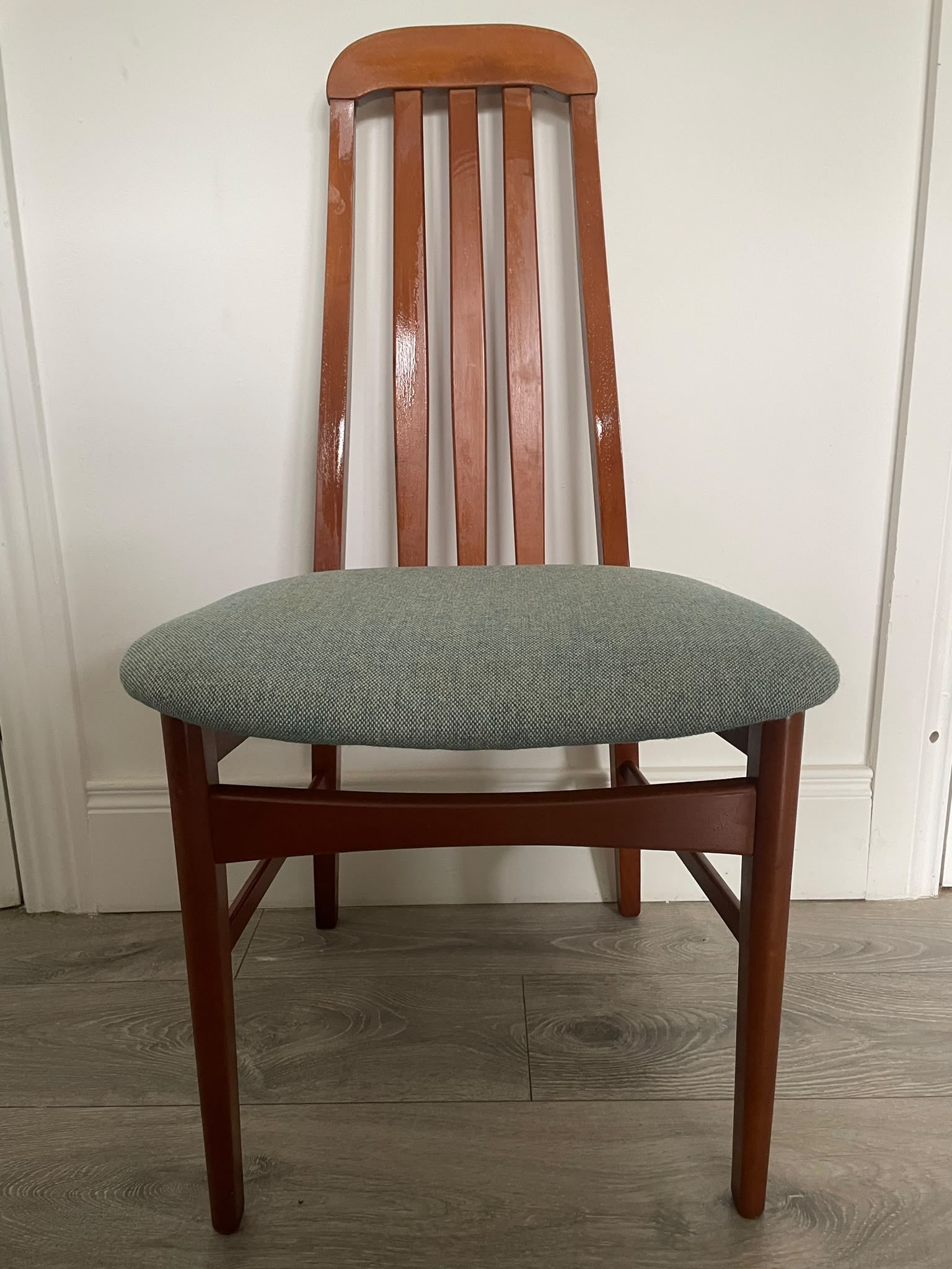 A wooden mid century Jenitique dining chair with a tall slatted backrest and a light blue upholstered seat cushion, shown on a gray wood floor against a white wall by Grace & Joy Furniture