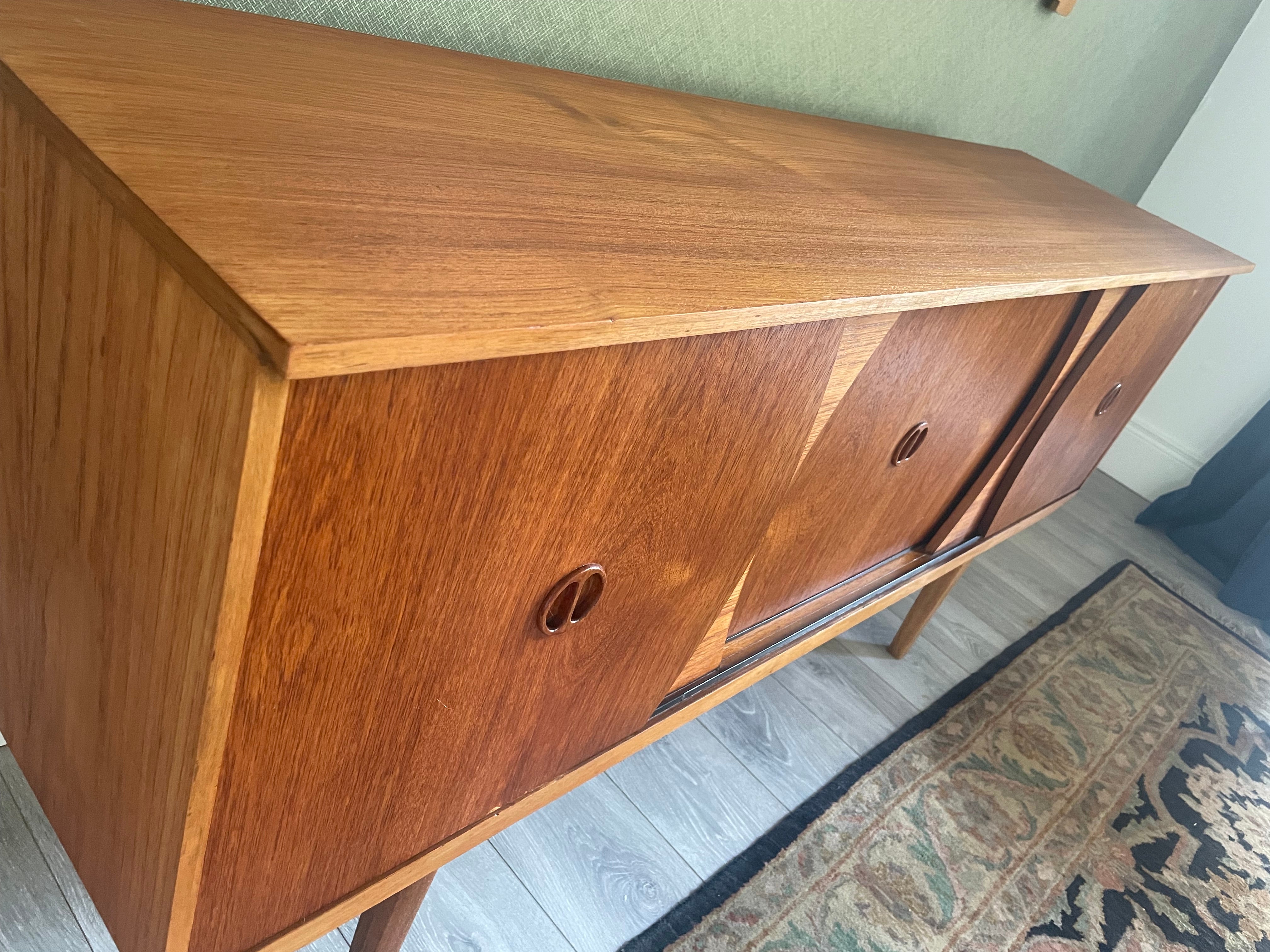Restored mid-century modern wooden credenza or cabinet with three curved doors and circular pull handles, photographed in a home interior with wood flooring and a patterned rug visible by Grace & Joy Furniture