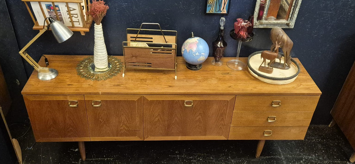 A mid-century modern wooden sideboard cabinet with six drawers, styled with various decorative objects against a dark blue wall.