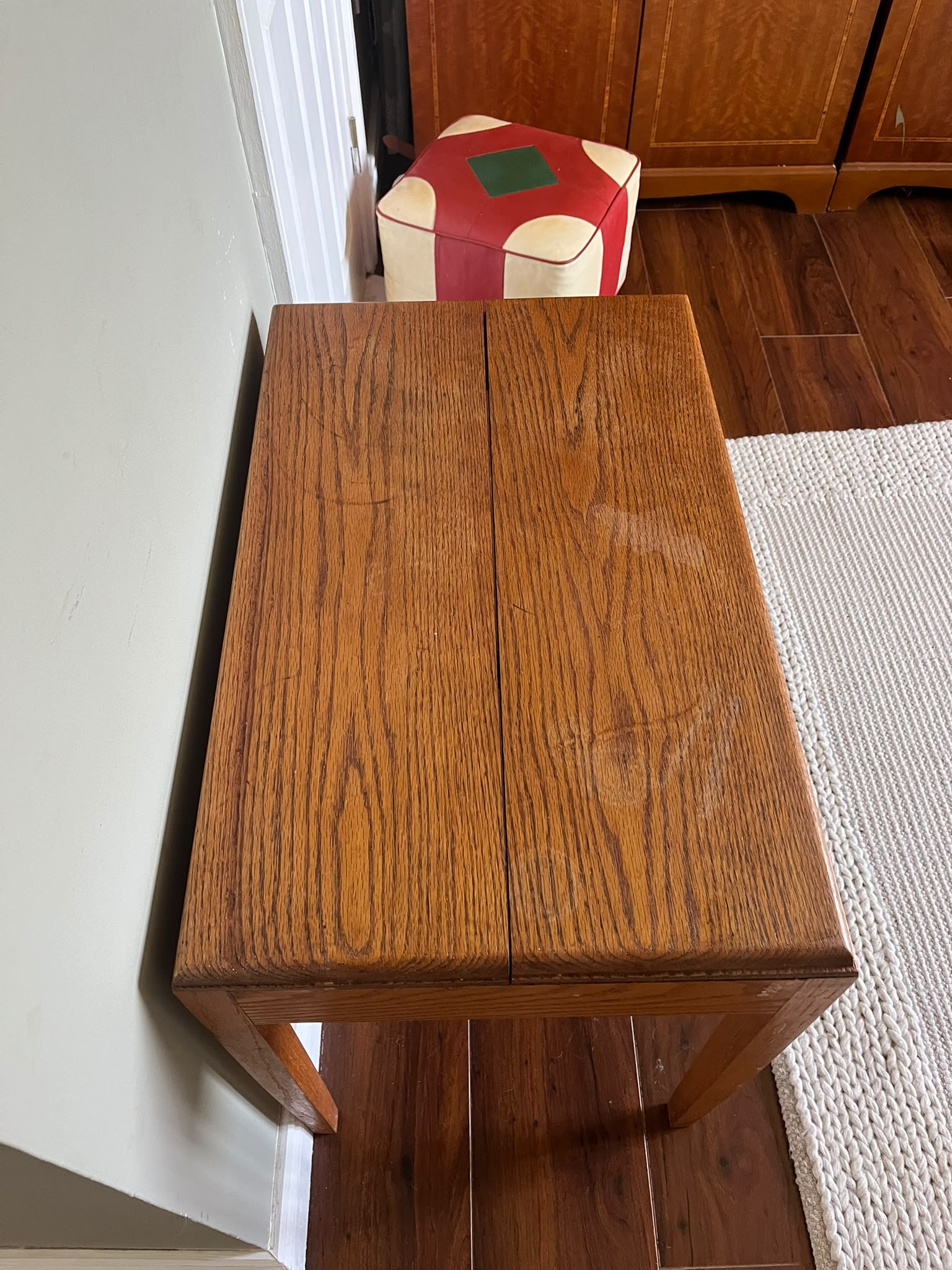 A mid-century modern wooden side table with a warm medium-brown finish, styled with a green pleated table lamp and a stack of books in a room with dark wood floors and a sage green wall by Grace & Joy furniture