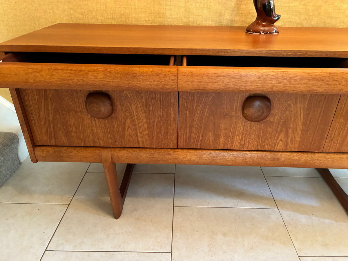 Mid-century modern wooden sideboard with two drawers featuring round knobs, shown on a tiled floor against a textured wall.
