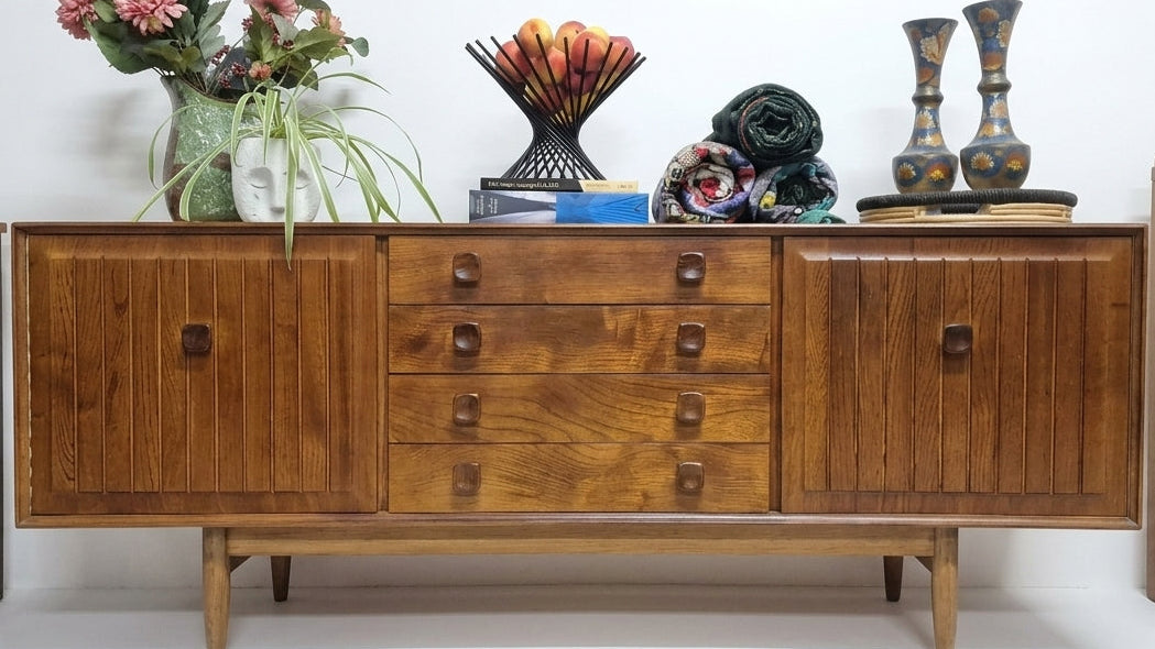 Mid-century modern wooden sideboard cabinet with six drawers and two cabinet doors, styled with decorative objects on top, shown in a room setting.