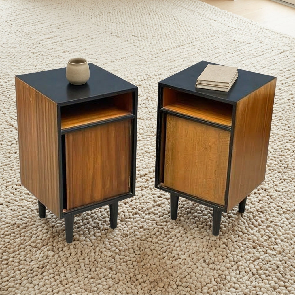 Two matching mid-century modern side tables with wood grain fronts, black tops and legs, shown on a textured beige rug with small decorative props on top.