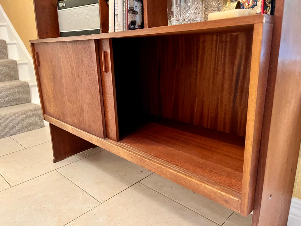 A mid-century modern wooden room divider or bookcase with a warm reddish-brown finish, styled with books, a small plant, and a hanging green leafy vine in a home interior.