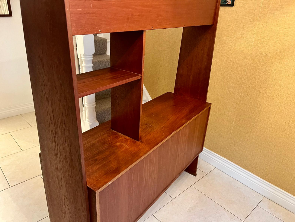 A mid-century modern wooden room divider or bookcase with a warm reddish-brown finish, styled with books, a small plant, and a hanging green leafy vine in a home interior.