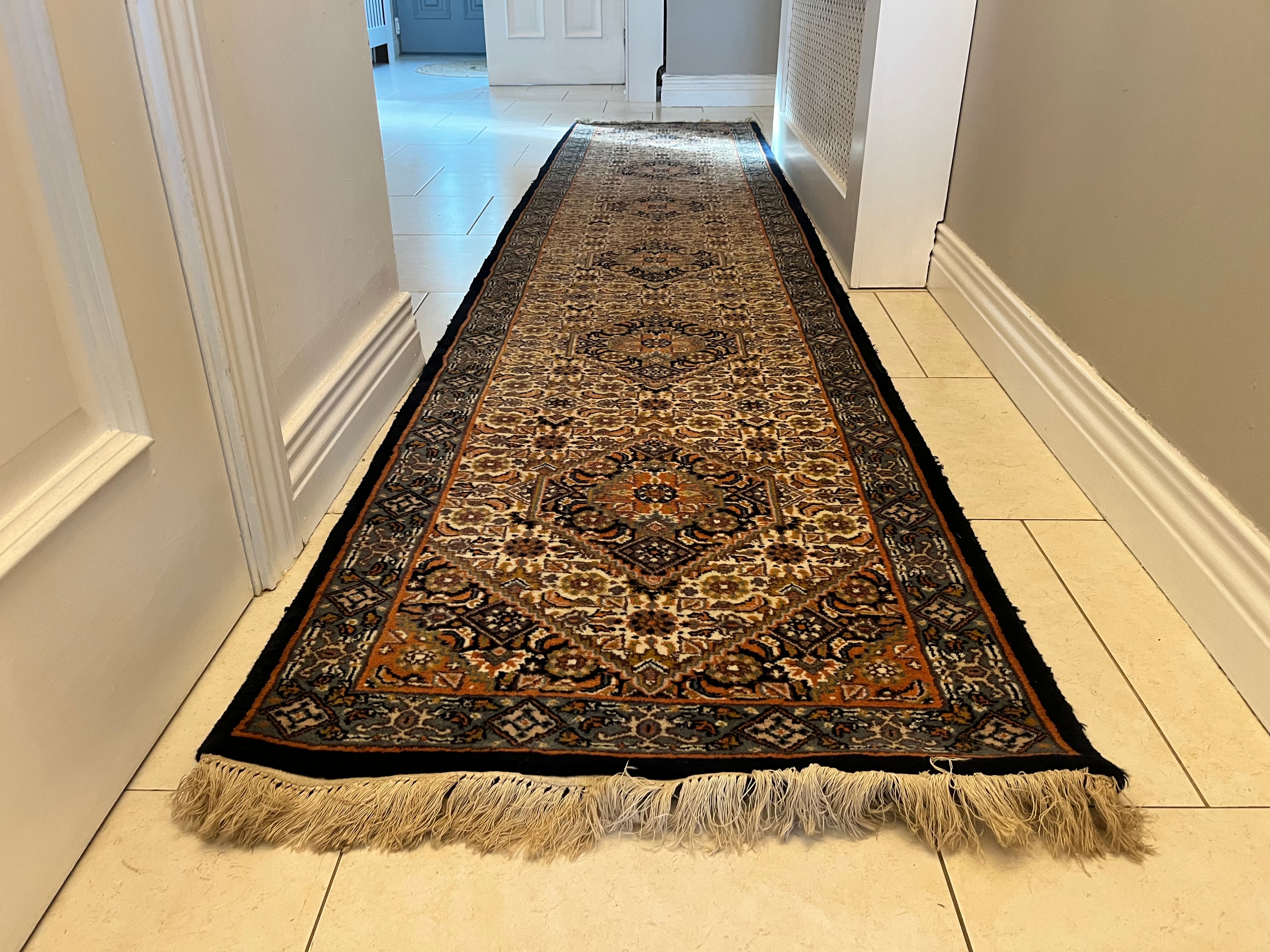A long traditional vintage runner rug with beige and black fringe, displayed on a light tiled hallway floor y Grace & Joy Furniture