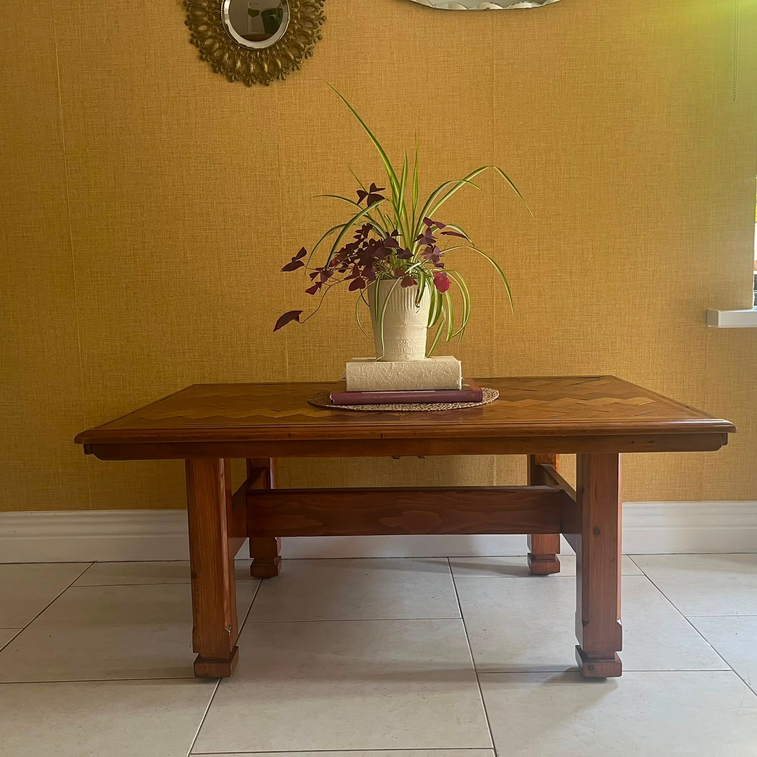 A Herringbone wooden coffee table with a geometric parquet inlay design on the top, set against a textured yellow wall and light-colored tiled floor by Grace & Joy Furniture
