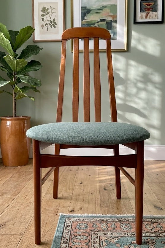 A wooden mid century Jenitique dining chair with a tall slatted backrest and a light blue upholstered seat cushion, shown on a gray wood floor against a white wall by Grace & Joy Furniture
