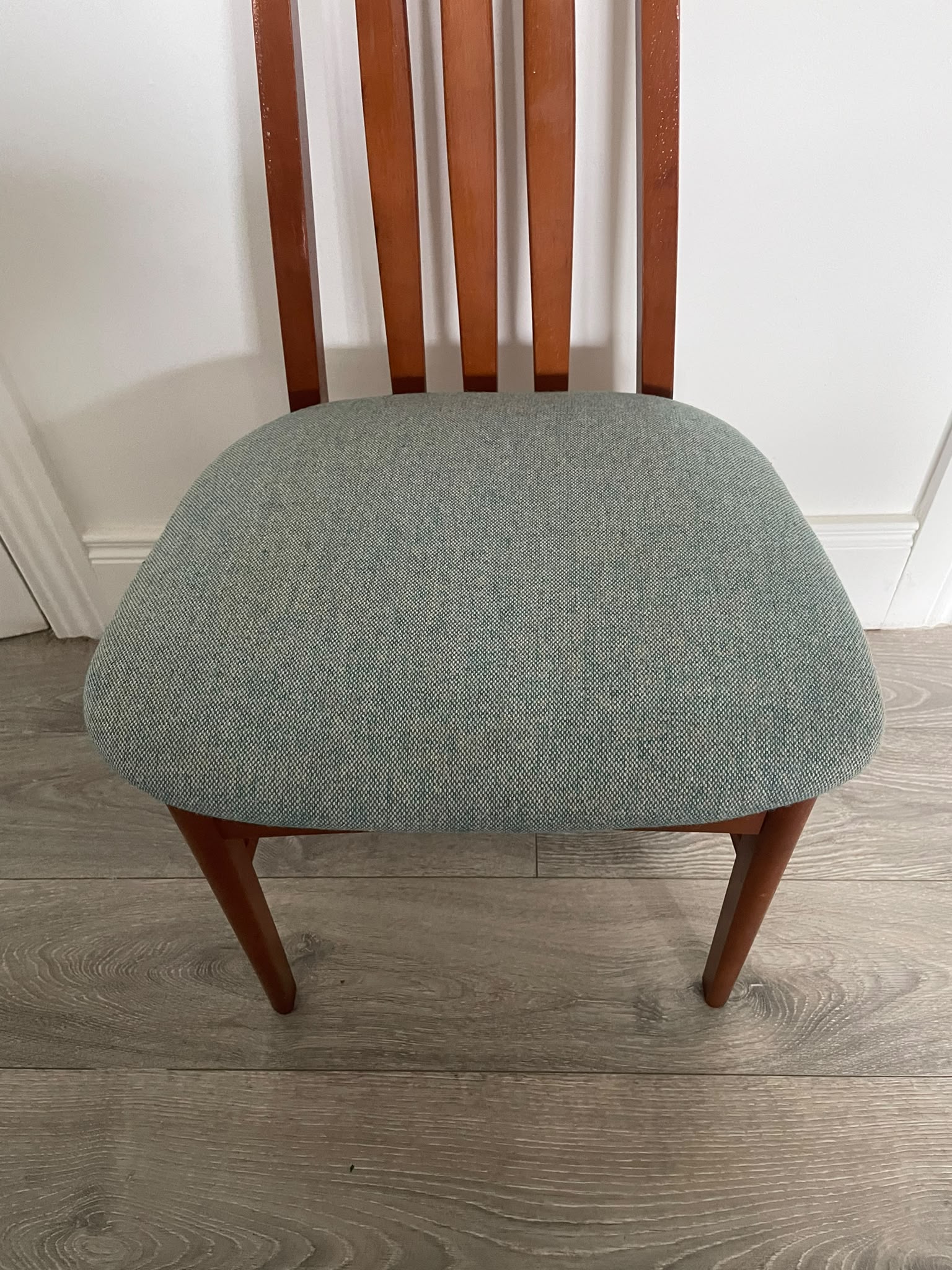 A wooden mid century Jenitique dining chair with a tall slatted backrest and a light blue upholstered seat cushion, shown on a gray wood floor against a white wall by Grace & Joy Furniture