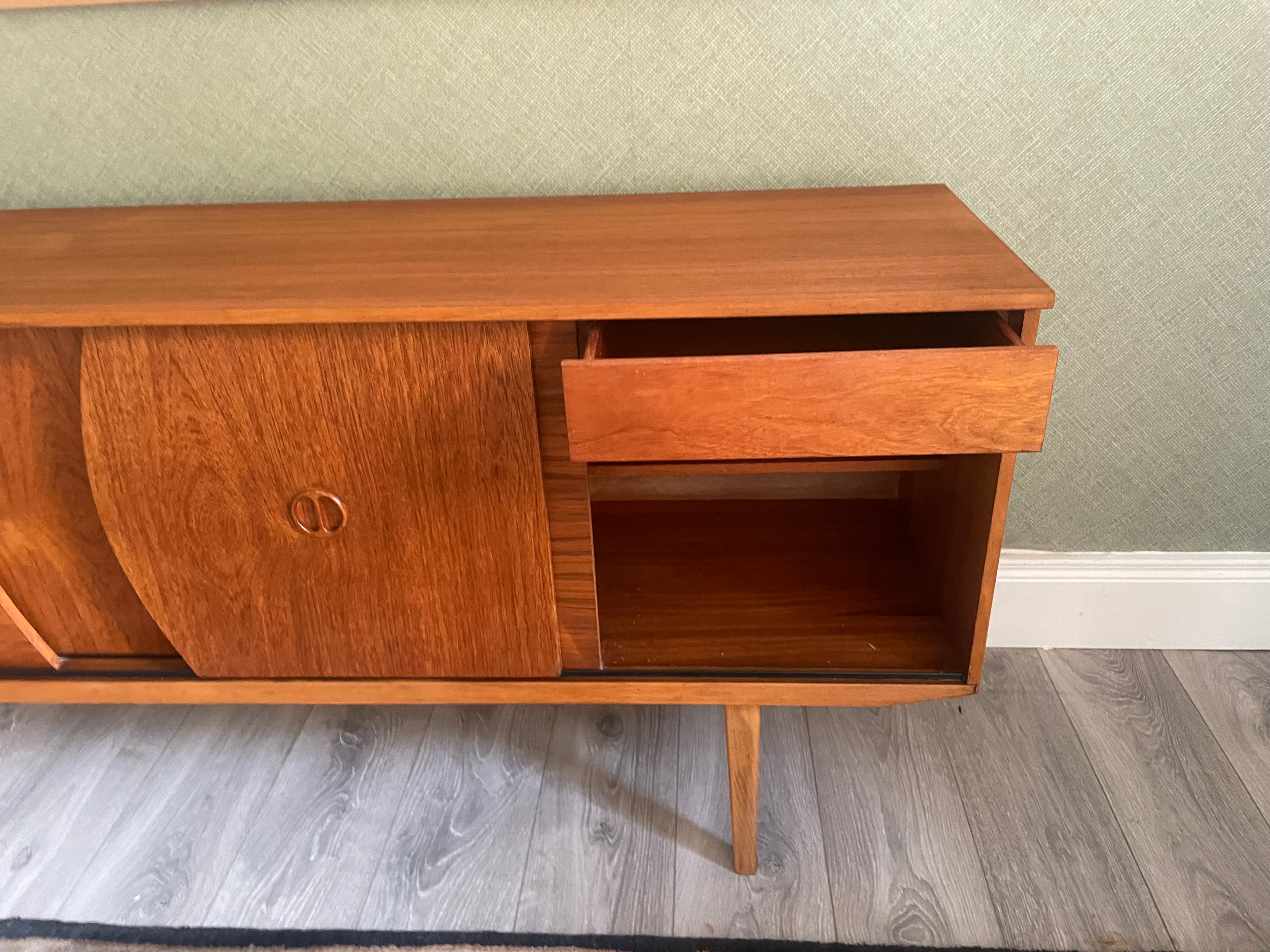 Restored mid-century modern wooden credenza or cabinet with three curved doors and circular pull handles, photographed in a home interior with wood flooring and a patterned rug visible by Grace & Joy Furniture