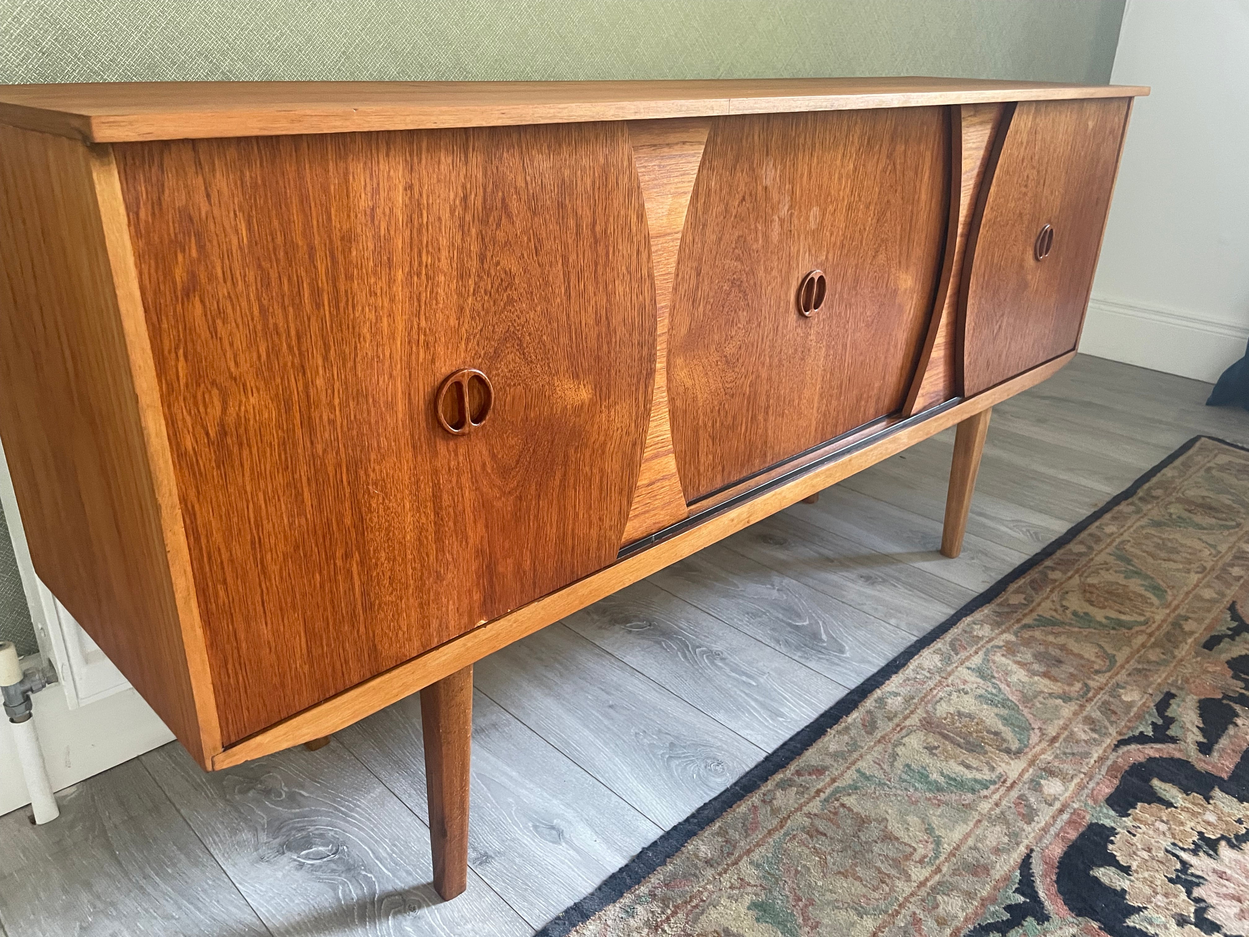 Restored mid-century modern wooden credenza or cabinet with three curved doors and circular pull handles, photographed in a home interior with wood flooring and a patterned rug visible by Grace & Joy Furniture