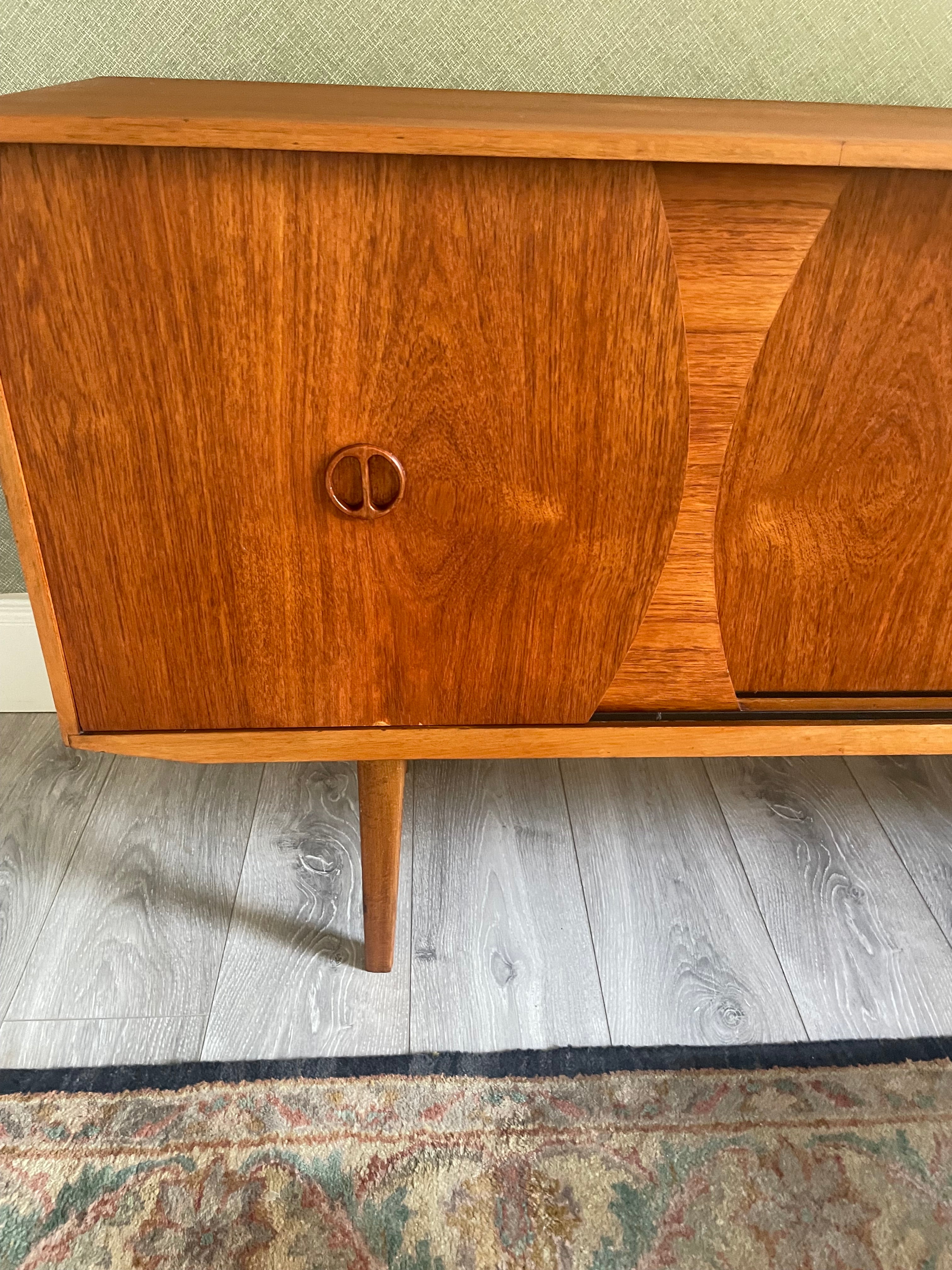 Restored mid-century modern wooden credenza or cabinet with three curved doors and circular pull handles, photographed in a home interior with wood flooring and a patterned rug visible by Grace & Joy Furniture