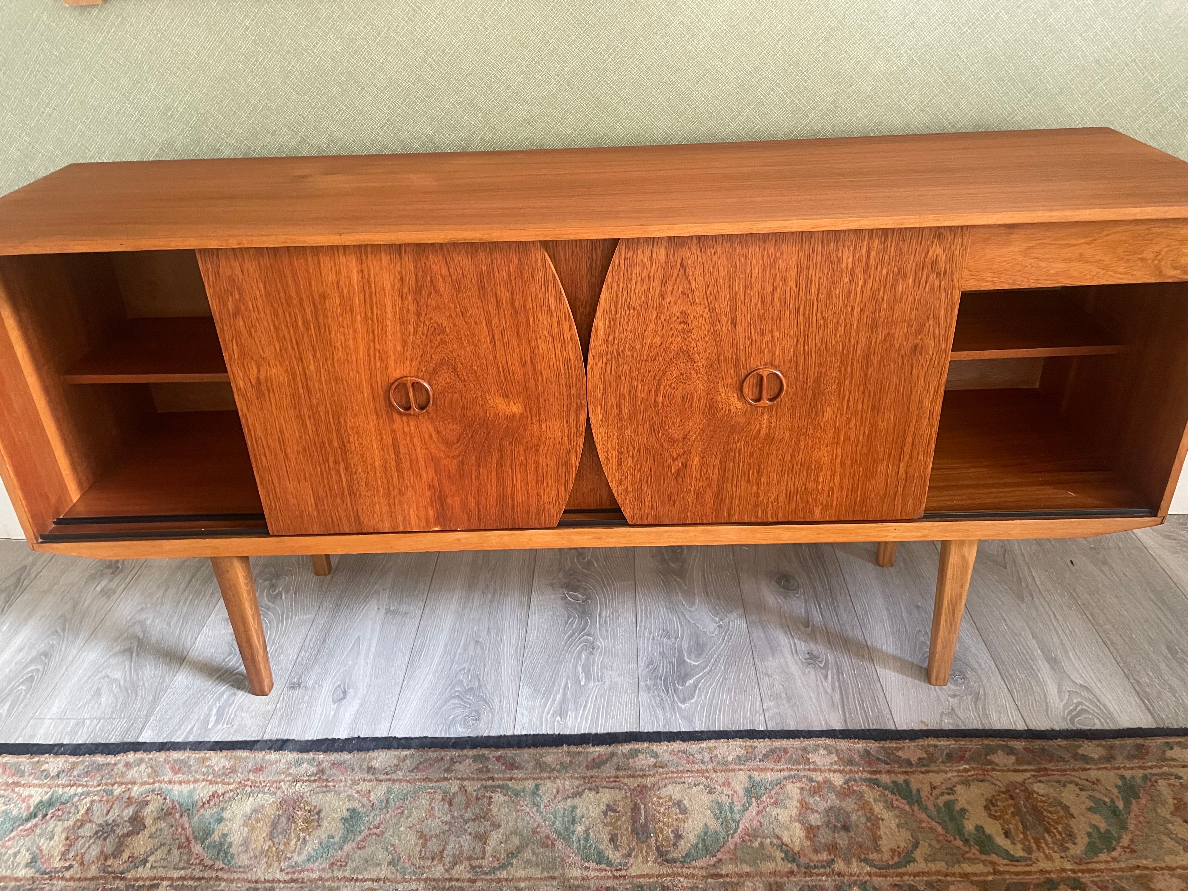 Restored mid-century modern wooden credenza or cabinet with three curved doors and circular pull handles, photographed in a home interior with wood flooring and a patterned rug visible by Grace & Joy Furniture