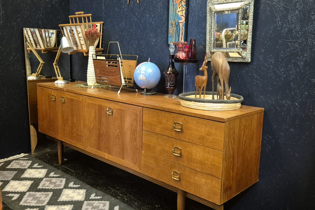A mid-century modern wooden credenza or sideboard with six drawers and a wood-grain cabinet, styled with various decorative objects against a dark blue textured wall.