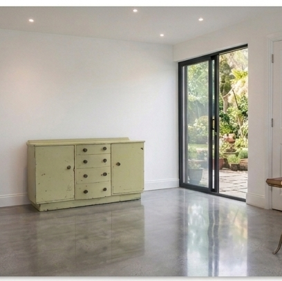A rustic light green wooden sideboard cabinet with multiple drawers and doors, set against a white wall in a modern room with polished concrete floors, a black-framed glass door, by Grace & Joy Furniture