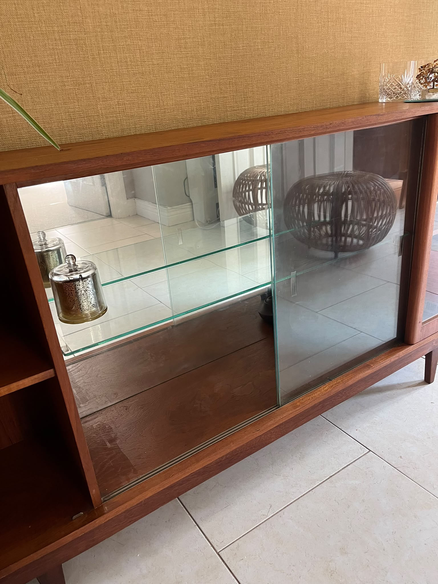 A mid-century modern SF Quinn wooden display cabinet with glass doors, shown in a home interior setting with tiled floors and textured walls by Grace & Joy Furniture