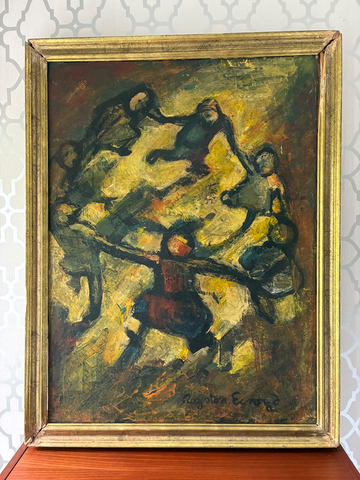 A framed Royston Ecroyd painting depicting figures in motion, signed ' at the bottom, housed in a gold-toned frame and displayed on a wooden surface against a patterned wallpaper background.