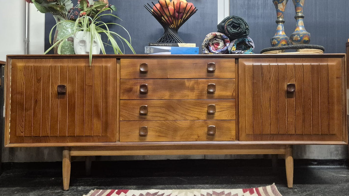 Mid-century modern wooden sideboard cabinet with three drawers and two doors, styled in a room setting with decorative vases and other furniture.