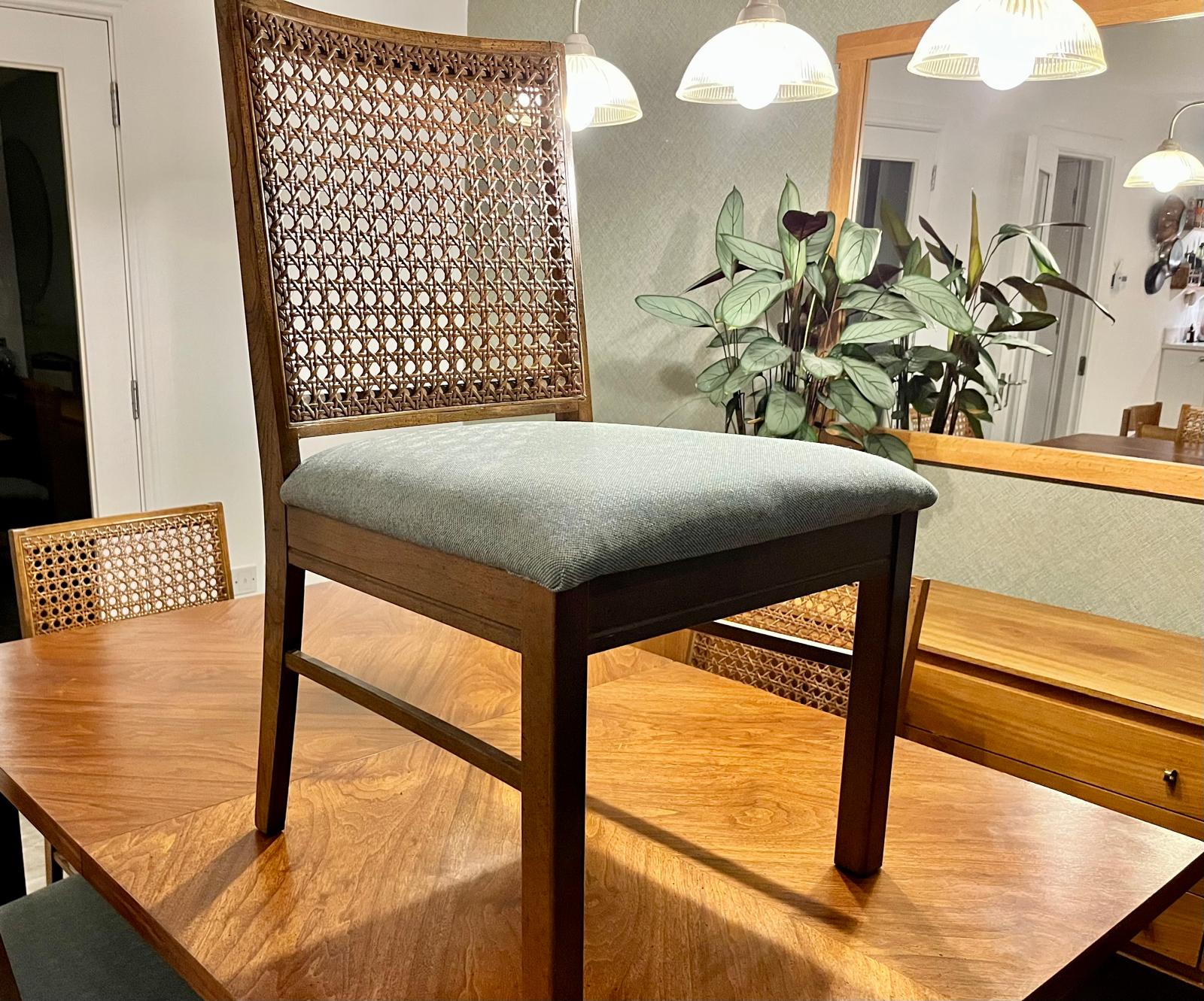 A wooden dining chair with a woven cane backrest and a light sage green upholstered seat cushion, shown on a wooden dining table in a home interior setting.